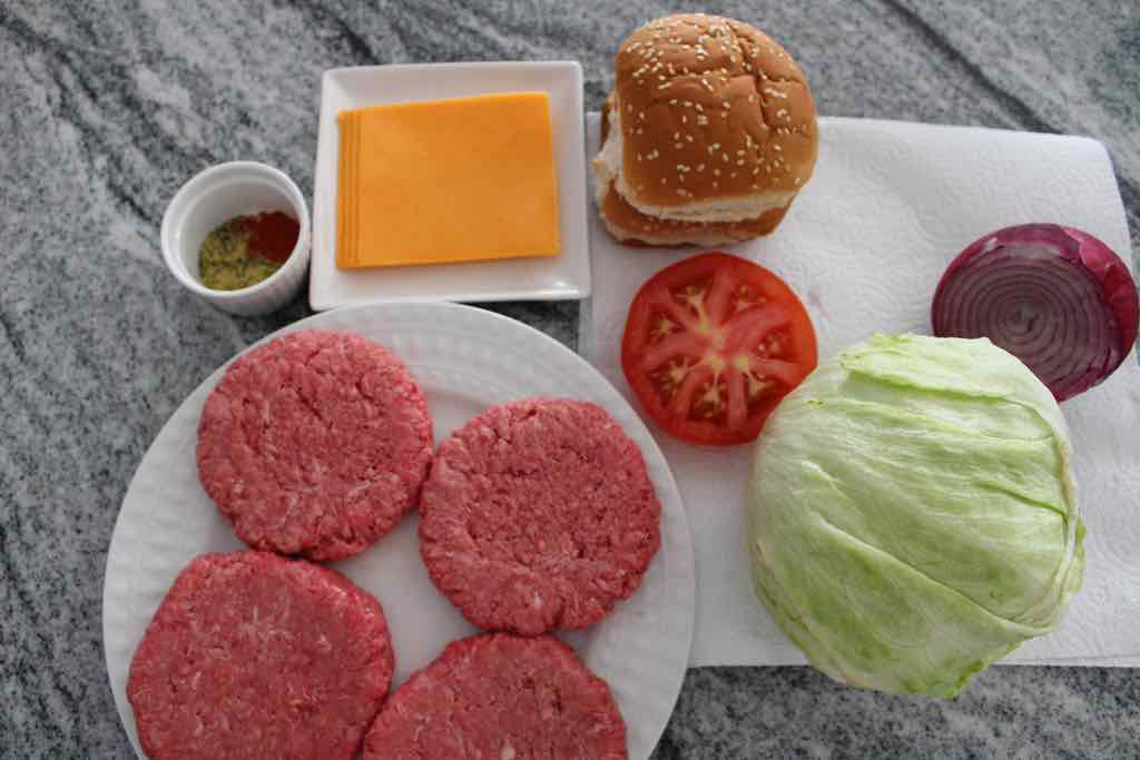 The ingredients to make instant pot hamburgers include ground beef, salt, pepper, smoked paprika, granulated garlic, cheddar cheese, lettuce, tomato, onions and ketchup.