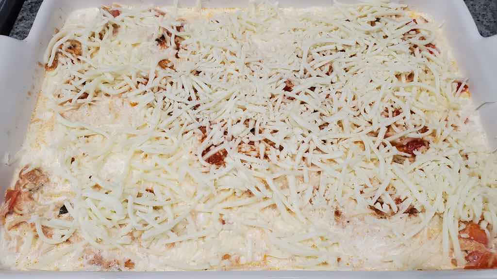 Topping the chicken lasagna with mozzarella and parmesan cheese.