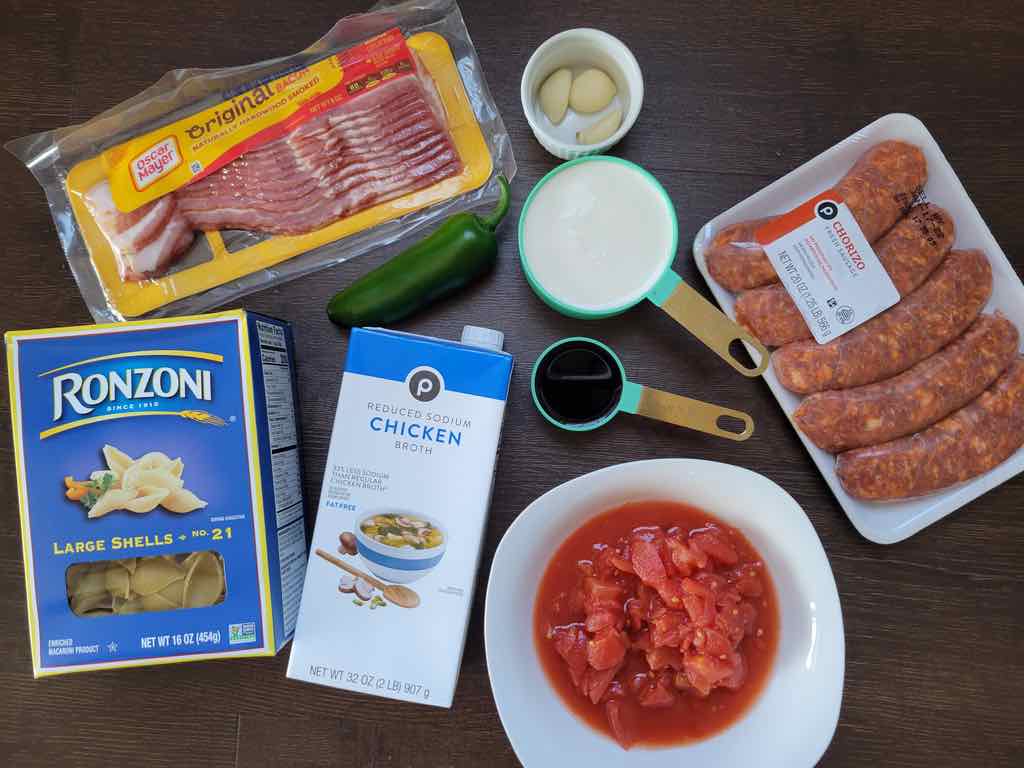The ingredients needed are pasta shells, chorizo sausage, bacon, red wine, heavy cream, diced tomatoes, tomato paste, chicken broth, garlic cloves, jalapeños and shaved parmesan cheese.