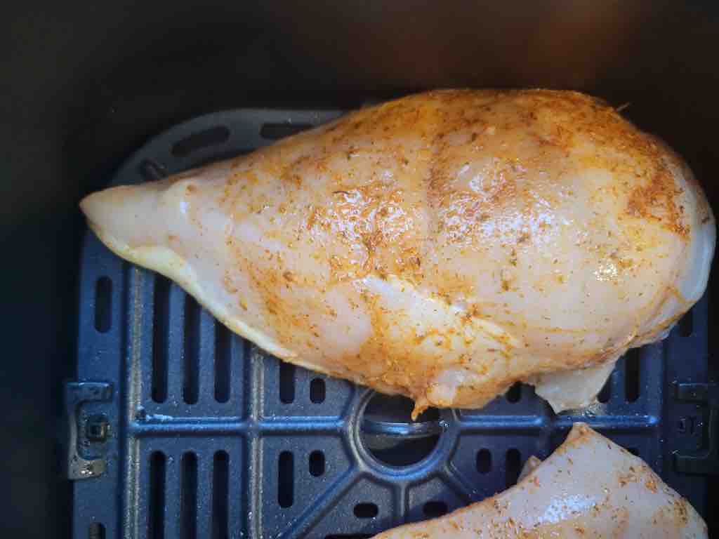 Season the chicken breasts on all sides with the dry rub and transfer to the air fryer to cook as shown in this photo.