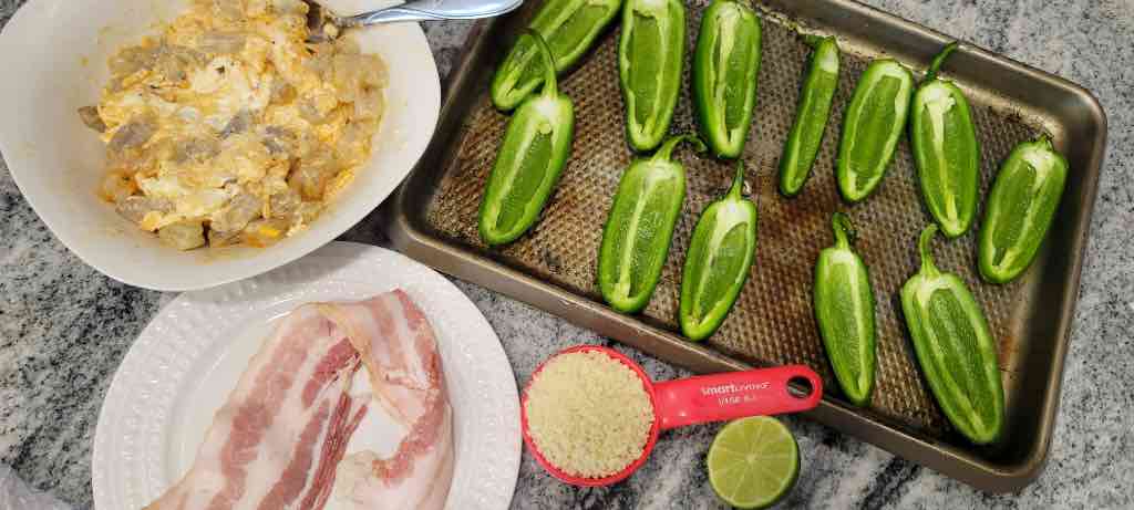 The ingredients needed are jalapeno peppers, shrimp, bacon, cream cheese, sharp cheddar cheese, garlic, lime juice, crushed red pepper flakes, salt, pepper, granulated garlic, paprika powder and Panko Bread Crumbs.