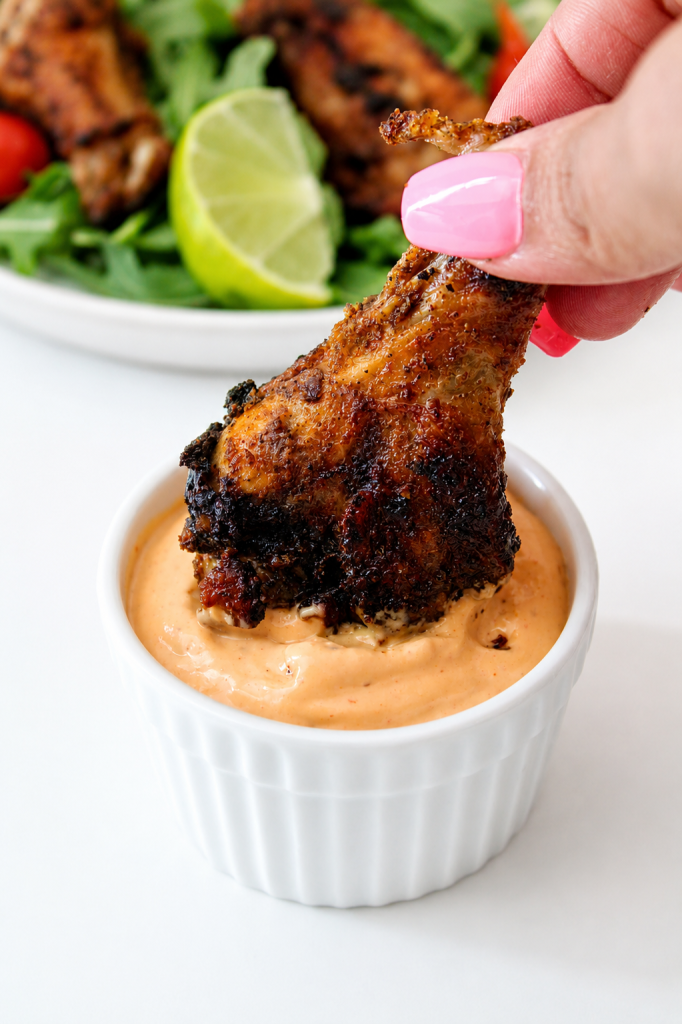 Blackened chicken wings being dipped in a spicy aioli sauce